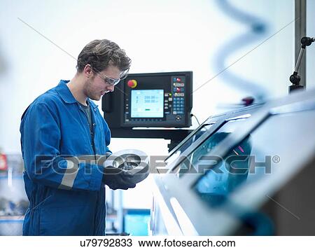 Stock Image - Apprentice engineer holding steel component with lathe in engineering factory. Fotosearch