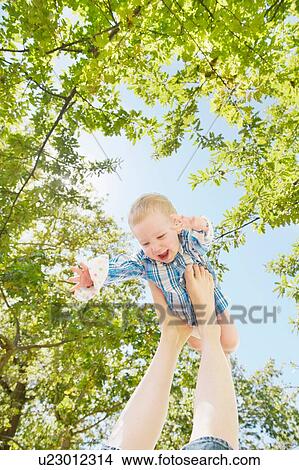 Picture - Baby boy balancing on top of mothers feet under blue sky. Fotosearch