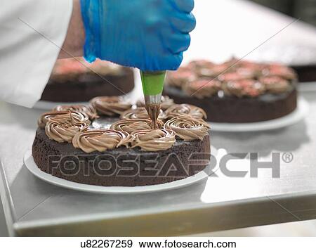 "Baker piping chocolate onto cakes in cake factory, close up" View Large Photo Image Stock Photo - "Baker piping chocolate onto cakes in cake factory, close up". Fotosearch