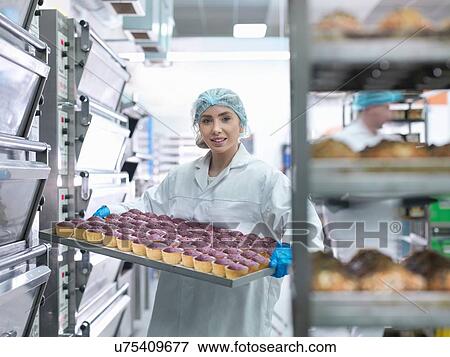 Stock Photo - "Baker taking cakes out of oven in cake factory, portrait". Fotosearch