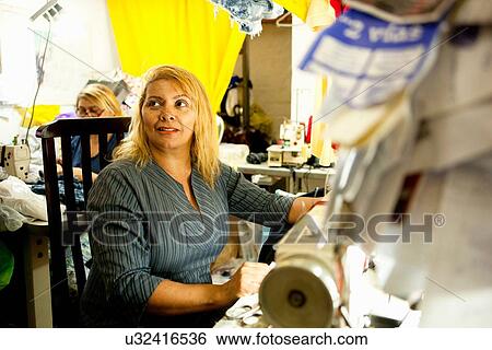 Stock Photograph - Board of receipts in front of two seamstresses sewing on machines in workshop. Fotosearch