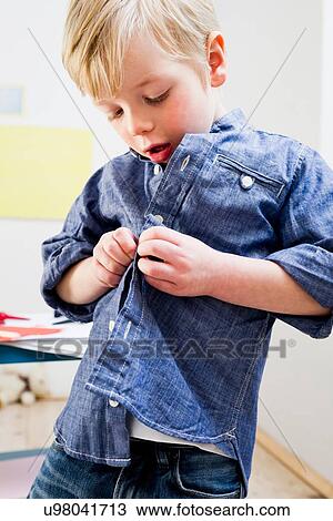 Stock Image - Boy buttoning shirt at home. Fotosearch
