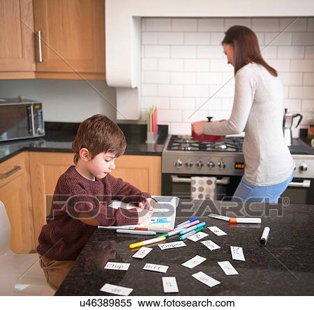 Boy coloring in book on kitchen counter as mother prepares dinner View Large Photo Image Stock Photography - Boy coloring in book on kitchen counter as mother prepares dinner. Fotosearch
