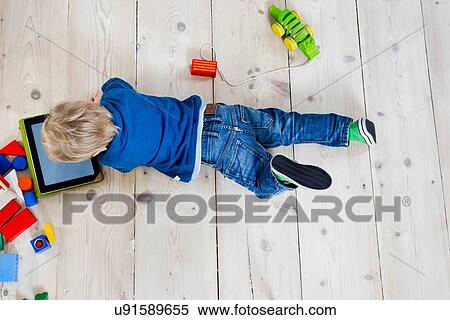 Boy playing with digital tablet on wooden floor View Large Photo Image Stock Photography - Boy playing with digital tablet on wooden floor. Fotosearch