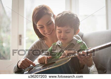 Boy sitting on mother's lap and learning to play guitar View Large Photo Image Stock Image - Boy sitting on mother's lap and learning to play guitar. Fotosearch