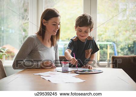 Boy smiling with mother as he paints on paper at table in living room View Large Photo Image Stock Photography - Boy smiling with mother as he paints on paper at table in living room. Fotosearch