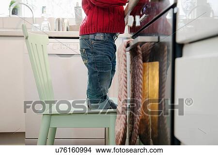 Picture - Boy standing on chair in kitchen. Fotosearch