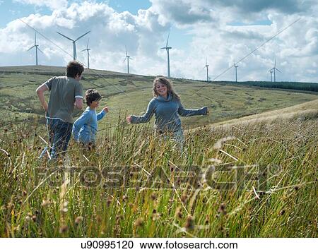 Stock Image - Brothers and sister running in long grass at windfarm. Fotosearch