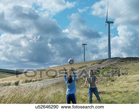 Stock Image - Brothers throwing football to each other with windfarm in background. Fotosearch