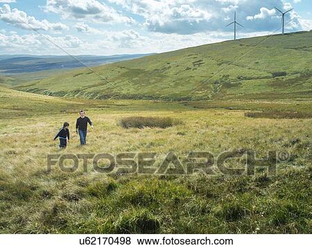 Stock Photo - Brothers walk up hill together at windfarm. Fotosearch