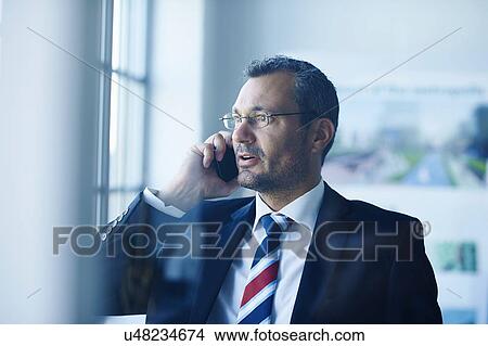 Business man chatting on smartphone whilst looking out of window View Large Photo Image Picture - Business man chatting on smartphone whilst looking out of window. Fotosearch