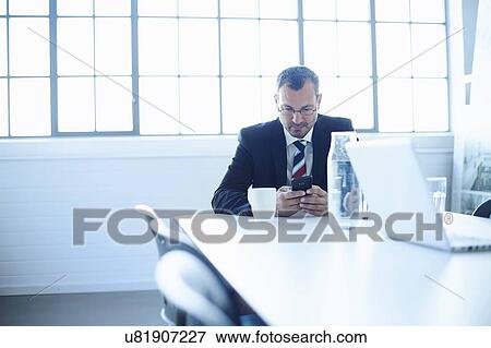 Business man reading smartphone texts at conference table View Large Photo Image Stock Photo - Business man reading smartphone texts at conference table. Fotosearch