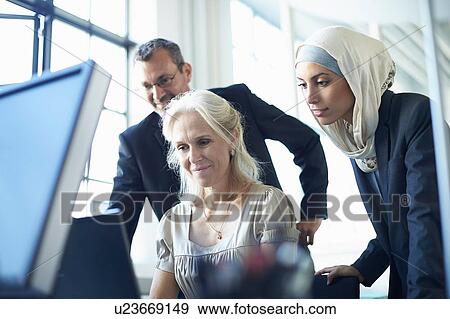 Business team looking at personal computer at office desk View Large Photo Image Stock Photo - Business team looking at personal computer at office desk. Fotosearch