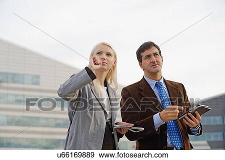Stock Photo - "Businessman and businesswoman outdoors, holding digital tablets, looking lost". Fotosearch