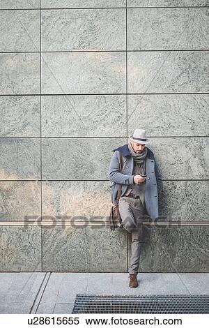 Stock Photography - Businessman leaning against wall texting on smartphone. Fotosearch