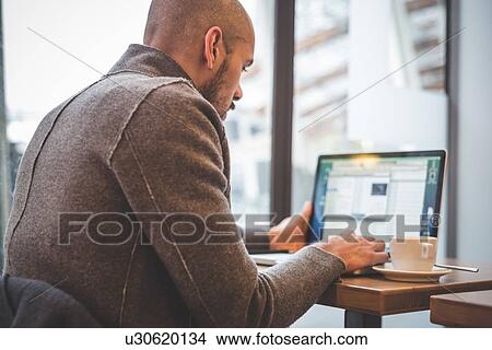 Businessman sitting in cafe typing on laptop View Large Photo Image Picture - Businessman sitting in cafe typing on laptop. Fotosearch
