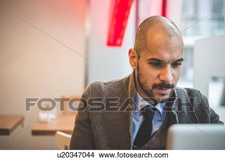 Businessman sitting in cafe using laptop View Large Photo Image Picture - Businessman sitting in cafe using laptop. Fotosearch