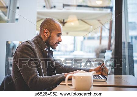 Stock Image - Businessman sitting in cafe working on laptop. Fotosearch