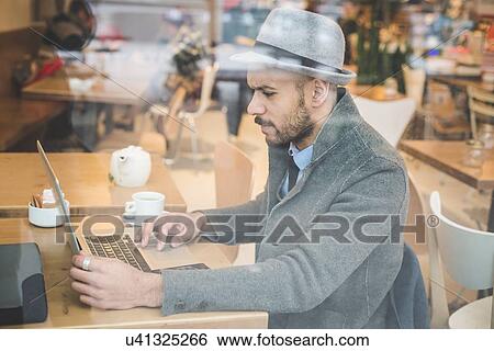 Businessman sitting in front of cafe window using laptop View Large Photo Image Stock Photograph - Businessman sitting in front of cafe window using laptop. Fotosearch