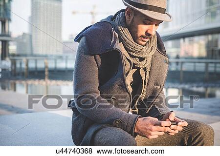 Stock Photo - Businessman sitting on wall texting on smartphone. Fotosearch