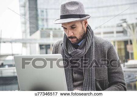 Stock Photo - Businessman sitting outside office using laptop. Fotosearch