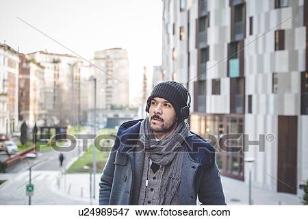 Stock Photo - Businessman walking along street and listening to headphones. Fotosearch