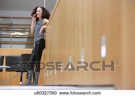 Stock Image - Businesswoman chatting on smartphone in office. Fotosearch