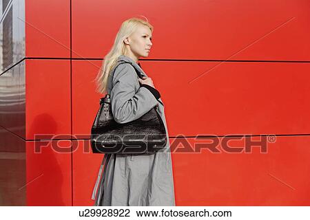 Stock Image - "Businesswoman, walking outdoors beside red building". Fotosearch
