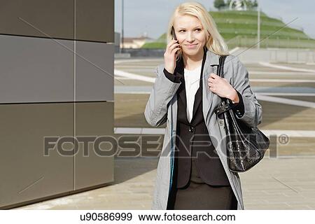 Stock Photo - "Businesswoman, walking outdoors, using mobile phone". Fotosearch