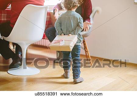 Stock Image - Child hiding surprise gift at family Christmas party. Fotosearch