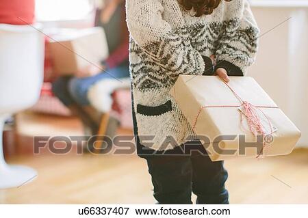 Stock Photo - Child hiding surprise gift at family Christmas party. Fotosearch