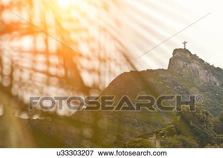 Stock Photo - "Christ the Redeemer Statue seen through palm fronds at sunset, RIo, Brazil". Fotosearch
