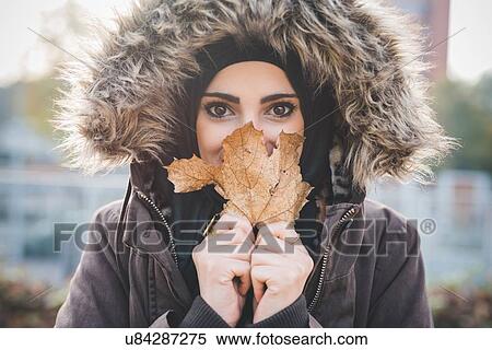 Close up of beautiful young woman in park holding up autumn leaf in front of face View Large Photo Image Stock Photography - Close up of beautiful young woman in park holding up autumn leaf in front of face. Fotosearch