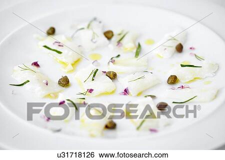Stock Photograph - "Close up of carpaccio of raw fish, capers and herbs on plate". Fotosearch