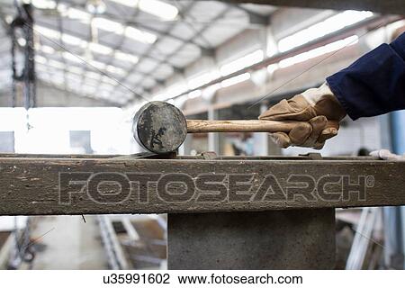 Stock Image - Close up of factory workers hand with rubber hammer in concrete reinforcement factory. Fotosearch
