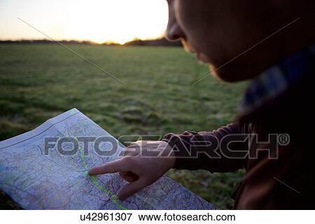 Stock Photo - Close up of male hiker pointing at map at sunset. Fotosearch