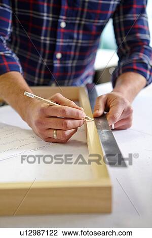 Stock Image - Close up of mid adult man measuring frame on workbench in picture framers workshop. Fotosearch