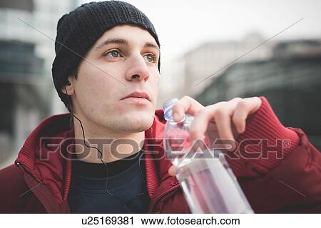 Stock Image - Close up of young man drinking water in city. Fotosearch