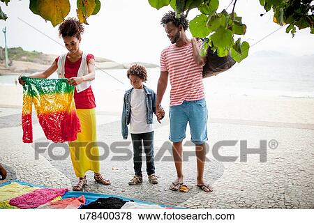 Stock Photo - "Couple and son choosing sweater from sidewalk stall, Ipanema beach, Rio De Janeiro, Brazil". Fotosearch