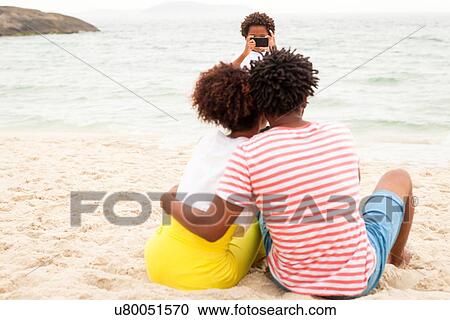 Stock Image - Couple and son taking photograph on beach. Fotosearch