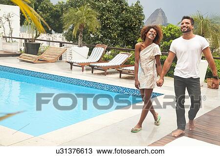 Stock Image - "Couple by terrace pool, Sugarloaf Mountain in background, Rio, Brazil". Fotosearch