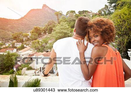 Stock Image - "Couple on terrace at sunset, Christ the Redeemer Statue in background, RIo, Brazil". Fotosearch