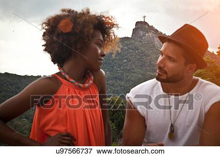 Stock Photo - "Couple on terrace at sunset, Christ the Redeemer Statue in background, RIo, Brazil". Fotosearch