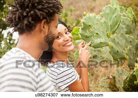 Stock Photo - "Couple pointing to names on cacti leaf, Ipanema beach, Rio De Janeiro, Brazil". Fotosearch