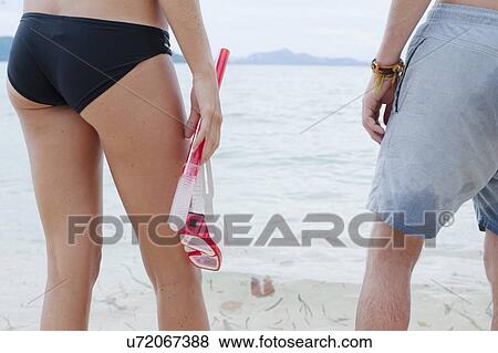 Stock Photo - "Cropped rear view of young couple holding snorkling goggles on beach, Kradan, Thailand". Fotosearch