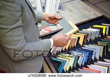 Stock Photo - Cropped shot of framer selecting frame in picture framers workshop. Fotosearch