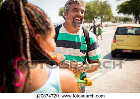 Stock Image - "Cropped shot of mature male skateboarder chatting on sidewalk, Copacabana, Rio De Janeiro, Brazil". Fotosearch