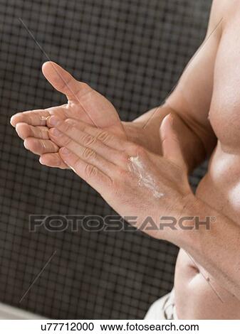 Stock Image - Cropped shot of muscular man in bathroom rubbing in hand cream. Fotosearch