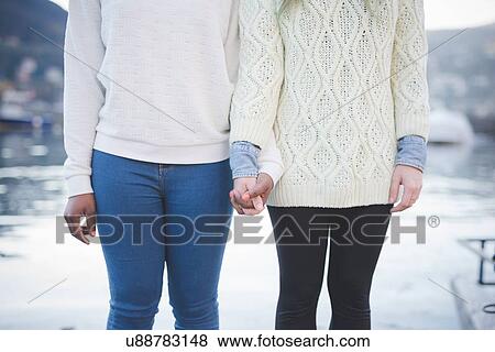 Stock Photo - "Cropped shot of two young female friends at lakeside, Lake Como, Italy". Fotosearch