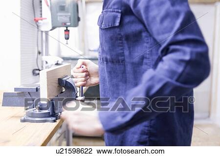 Stock Image - Cropped shot of young female carpenter putting timber in workshop vice. Fotosearch